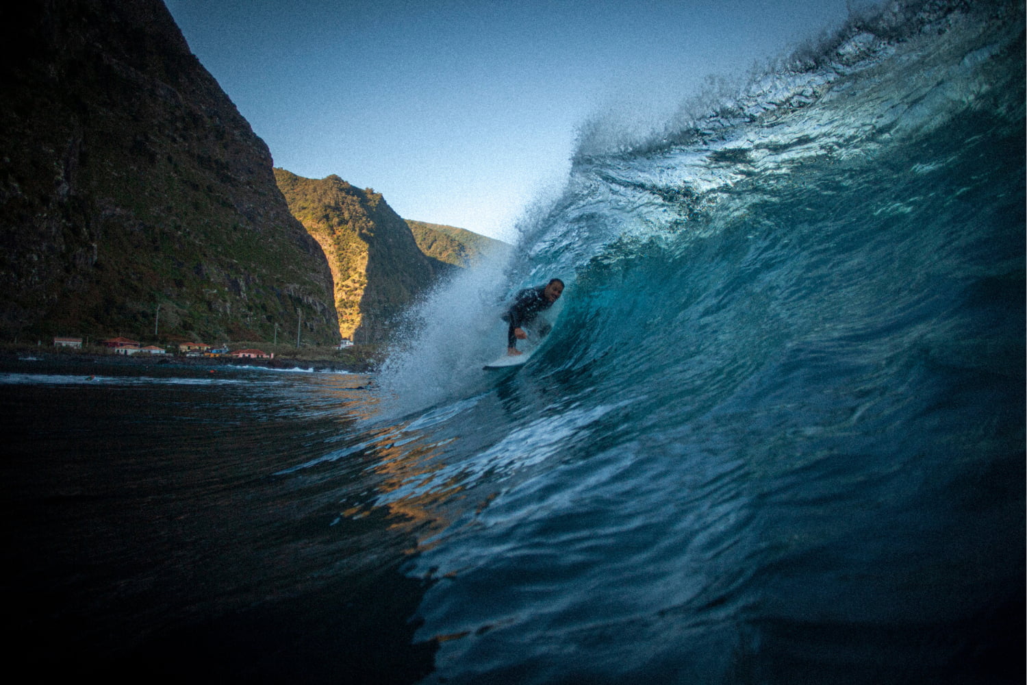 Surfer riding a blue, crystal wave in a volcanic beach with the help of the surf guiding in madeira he got