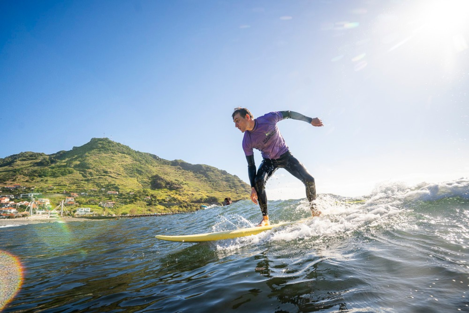 Male surfer riding a wave in machico in a sunny day while using a mid-length surfboard rented in madeira