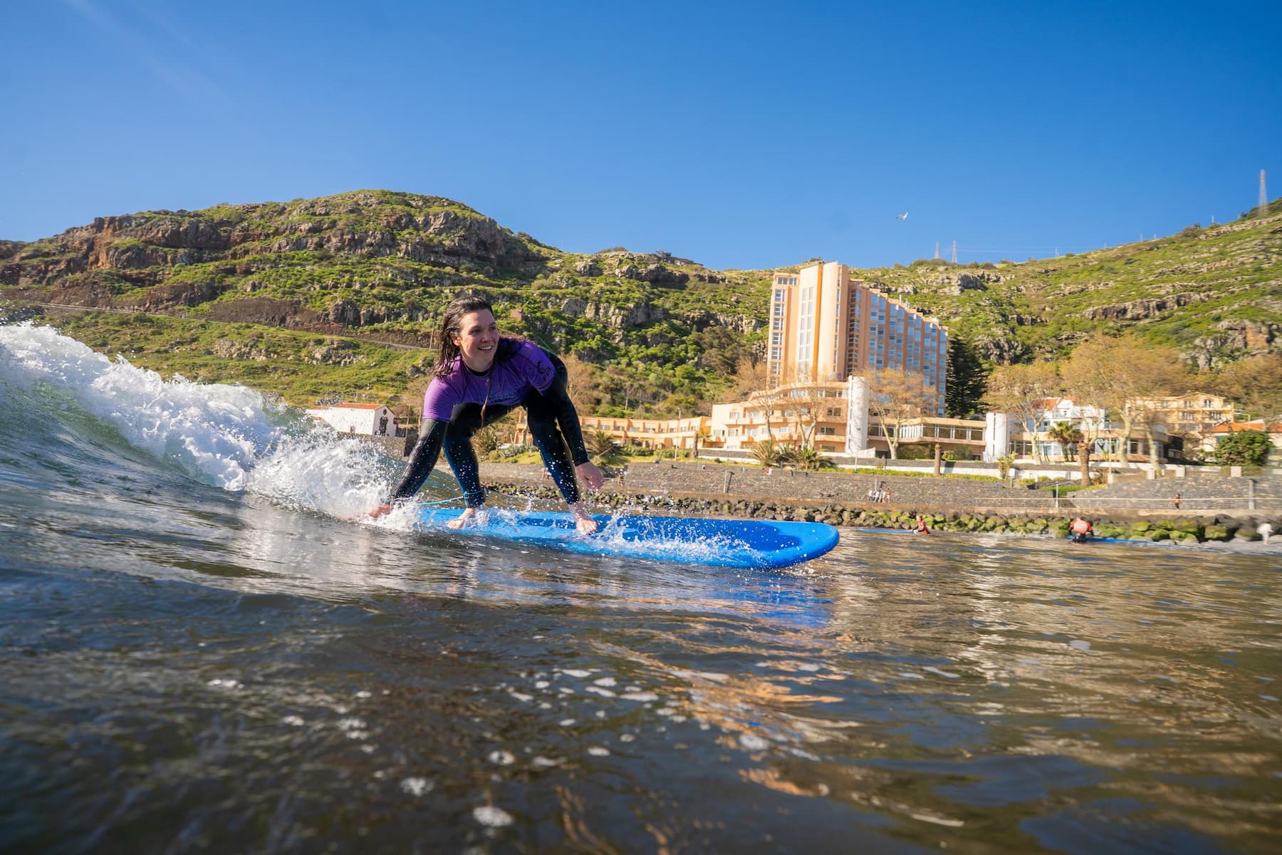 A happy female surfer riding a wave in Machico's beach while doing her surf lesson and using her rented surfboard in madeira