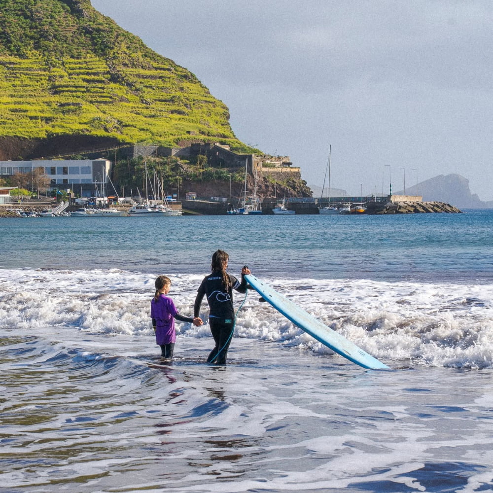 Surf instructor helping a kid in the water while doing surf lessons for kids in madeira