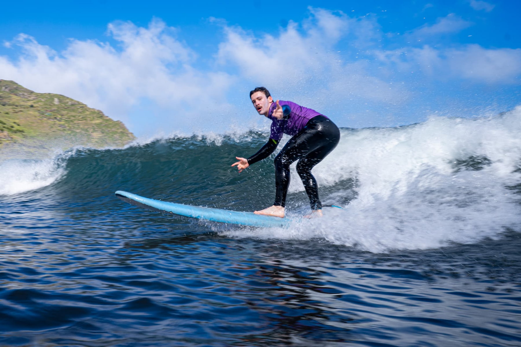Male surfer riding a blue wave in machico in a sunny day after getting the help of a surf guide in madeira